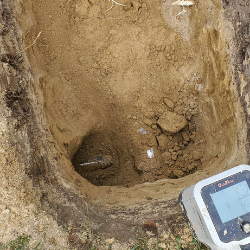 Technician using utility locating and testing equipment next to a ground excavation site