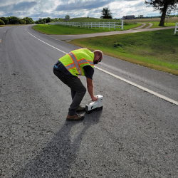 Technician performing ground-penetrating radar and utility locating on a paved road